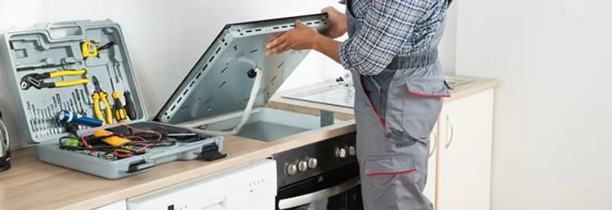 Cooktop repair technician lifting a built-in stovetop for service in Wilmington, NC