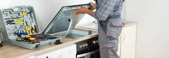 Cooktop repair technician lifting a built-in stovetop for service in Wilmington, NC