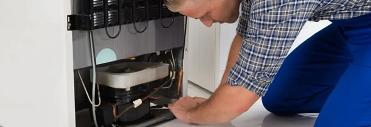 Refrigerator repair technician servicing the compressor and condenser area in Wilmington, NC