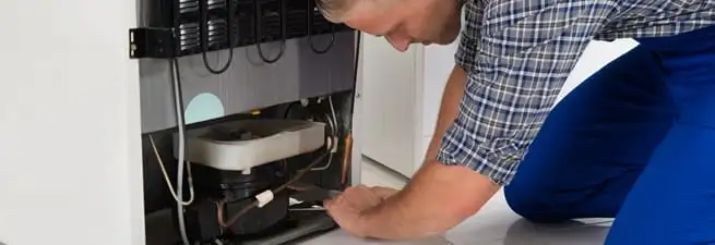 Refrigerator repair technician servicing the compressor and condenser area in Wilmington, NC
