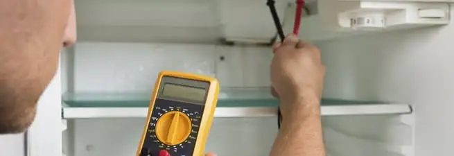 Refrigerator repair technician testing electrical components with a multimeter in Wilmington, NC