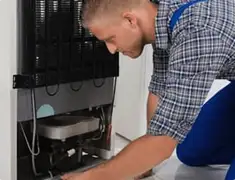 Refrigerator repair technician servicing the compressor and condenser area in Wilmington, NC
